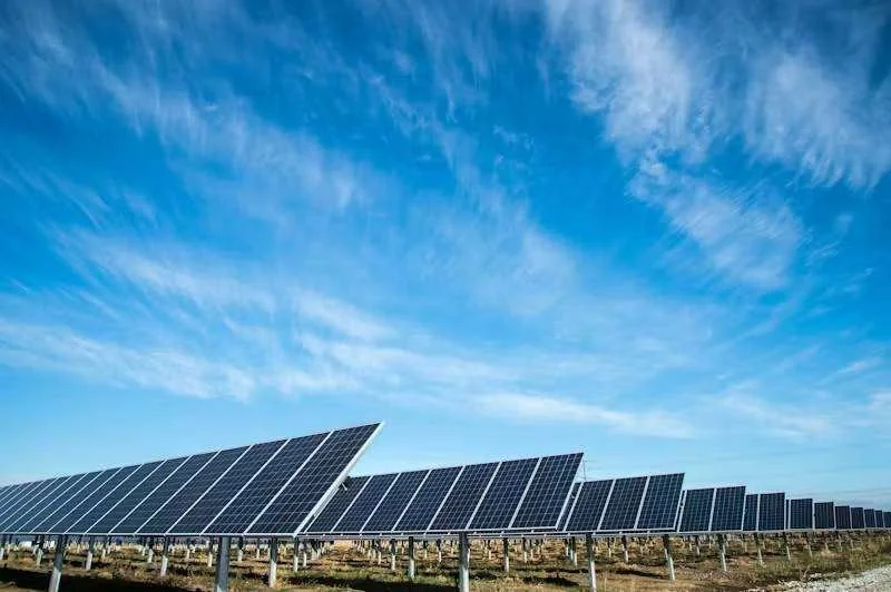 Usina solar com fileiras de painéis fotovoltaicos sob céu azul e nuvens