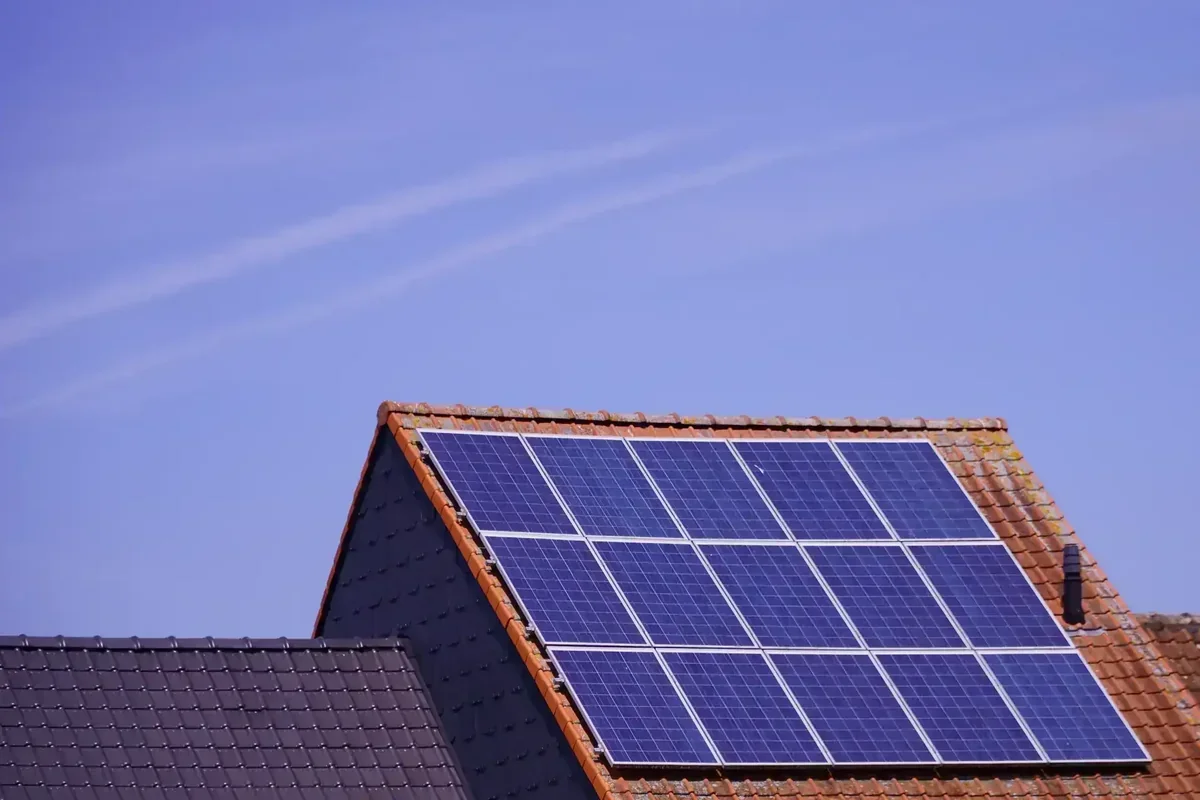 Sistema de energia solar em telhado de casa com telhas de cerâmica e céu azul claro