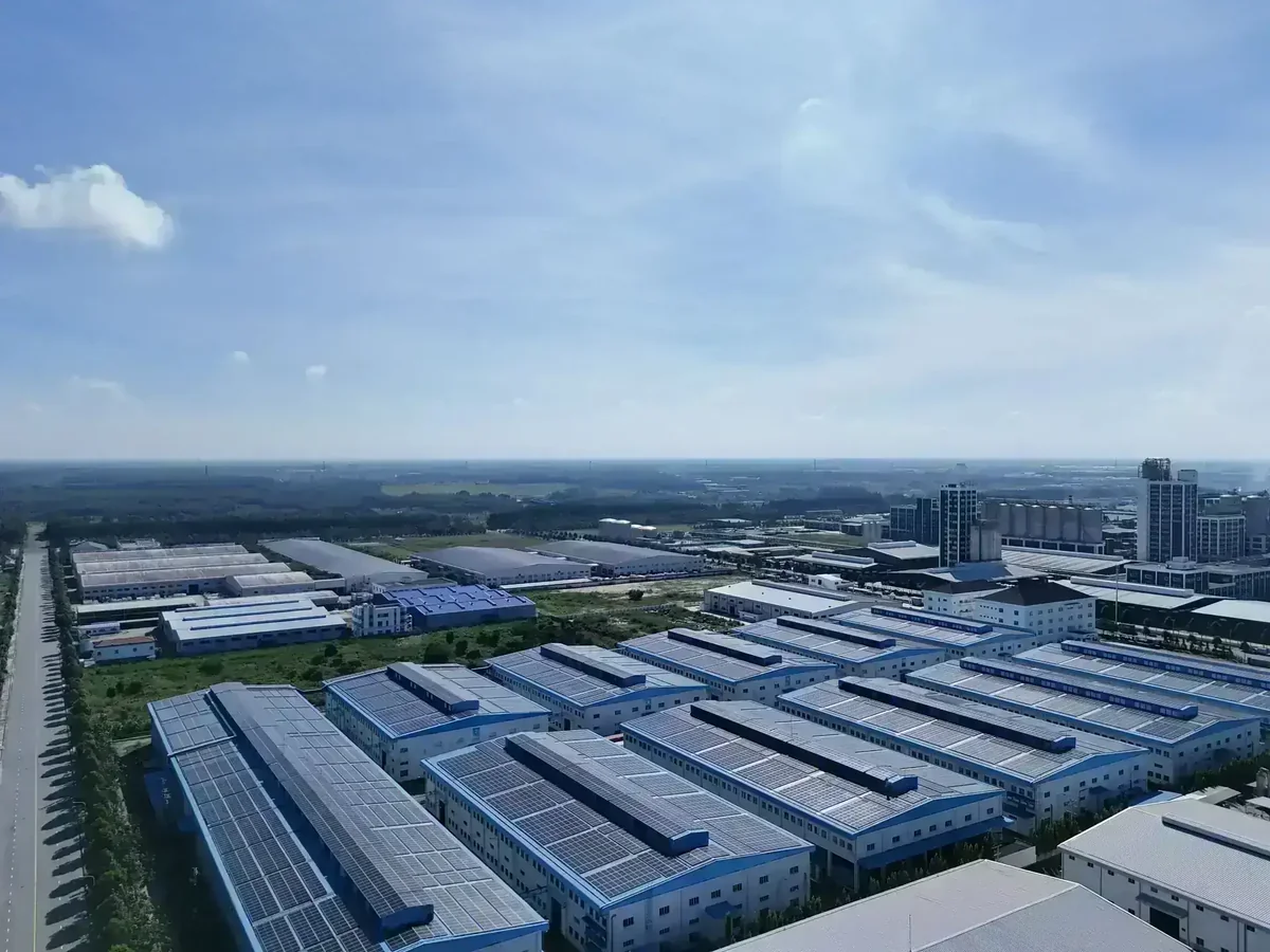 Vista aérea de complexo industrial com galpões e painéis solares nos telhados, sob céu azul