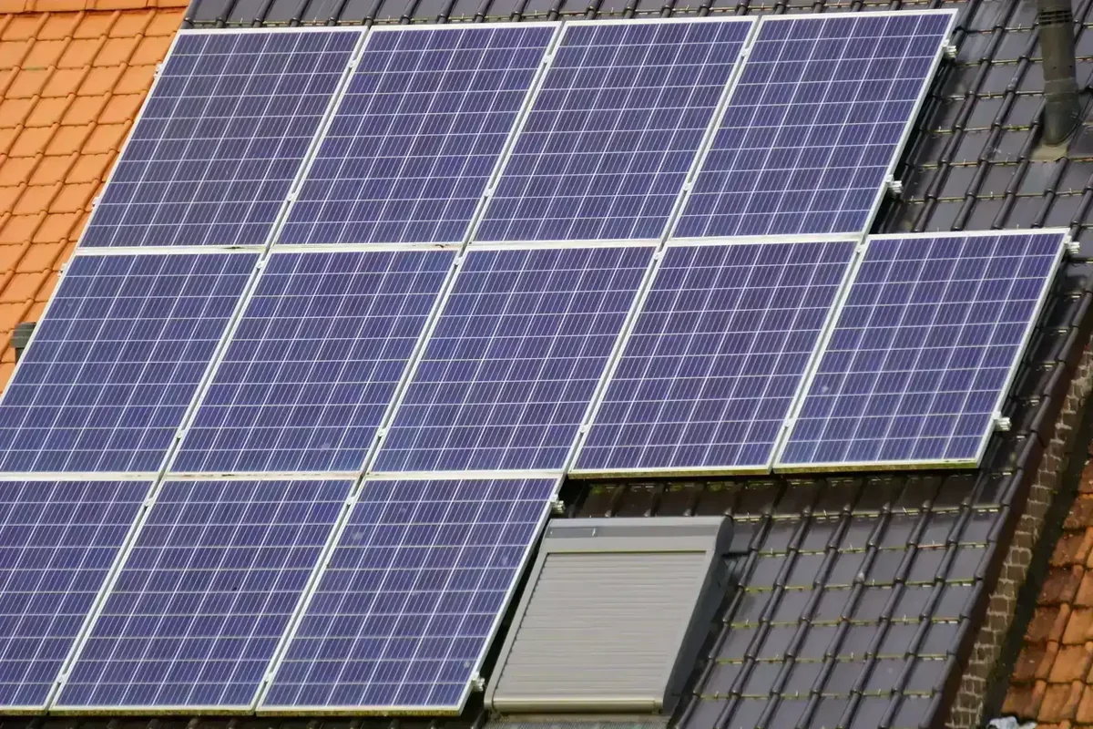 Painéis solares azuis instalados em telhado com telhas laranjas e escuras, e uma claraboia