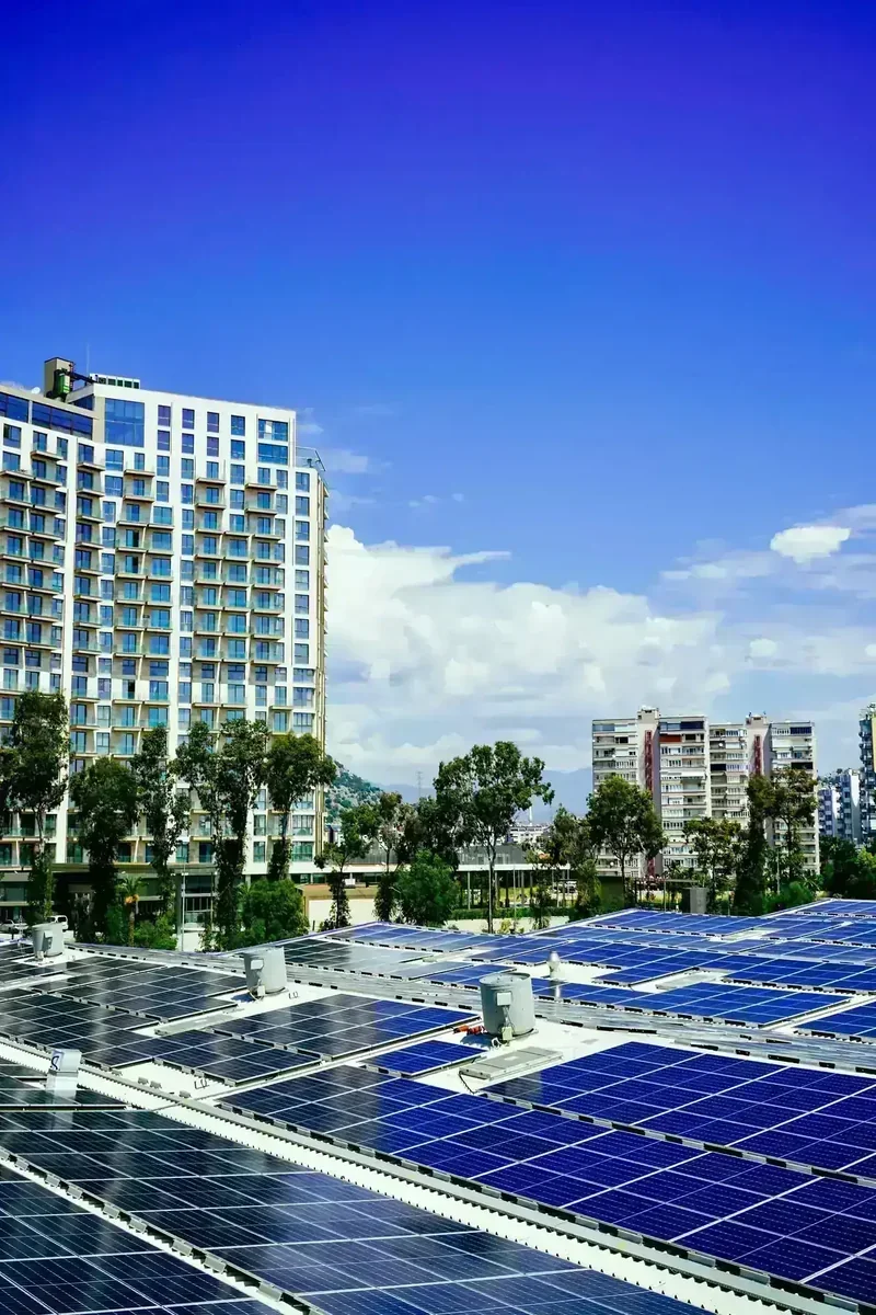 Painéis fotovoltaicos em telhado, com edifício moderno e outros prédios sob céu azul