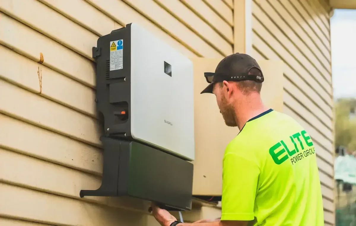 Homem instalando inversor solar Sungrow em parede de casa com revestimento bege