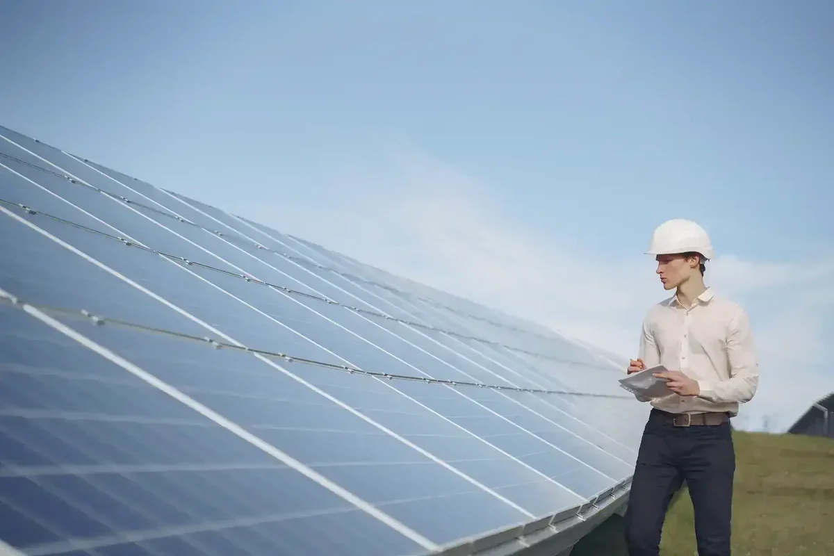 Homem de capacete branco inspeciona painéis solares sob céu azul