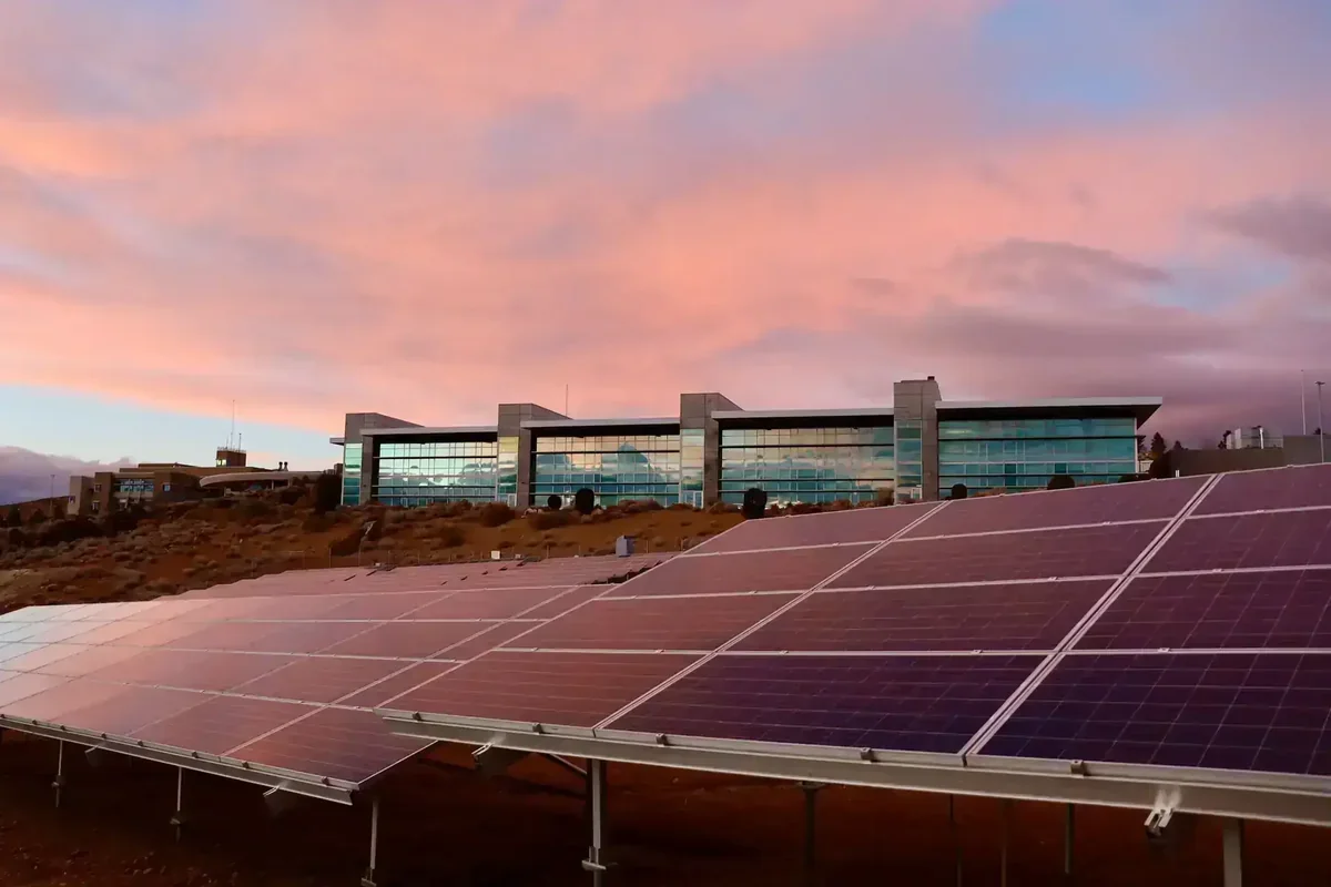Projeto de energia solar com painéis e edifício moderno sob céu rosado