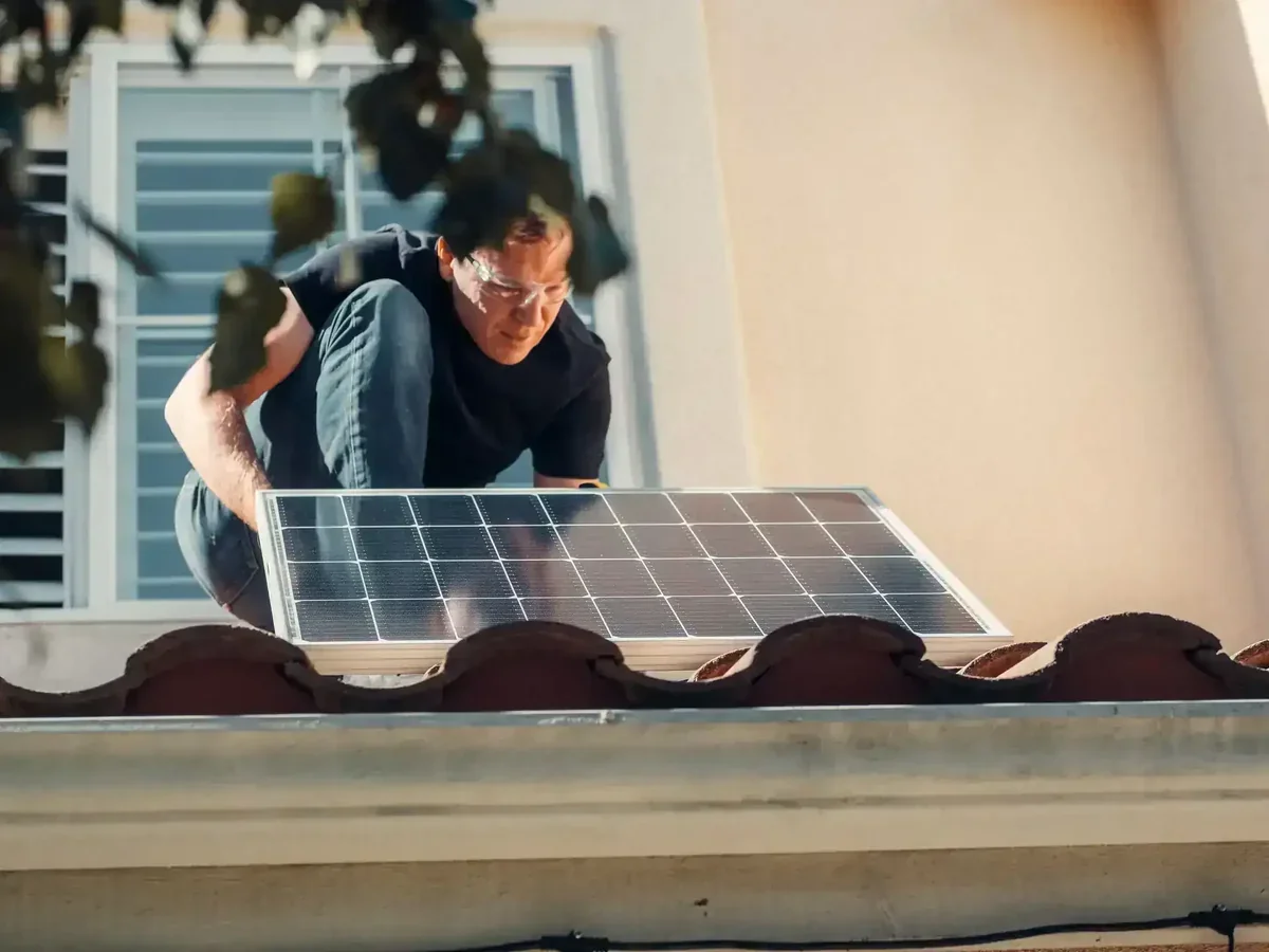 Homem instala painel solar em telhado de casa, usando óculos de segurança